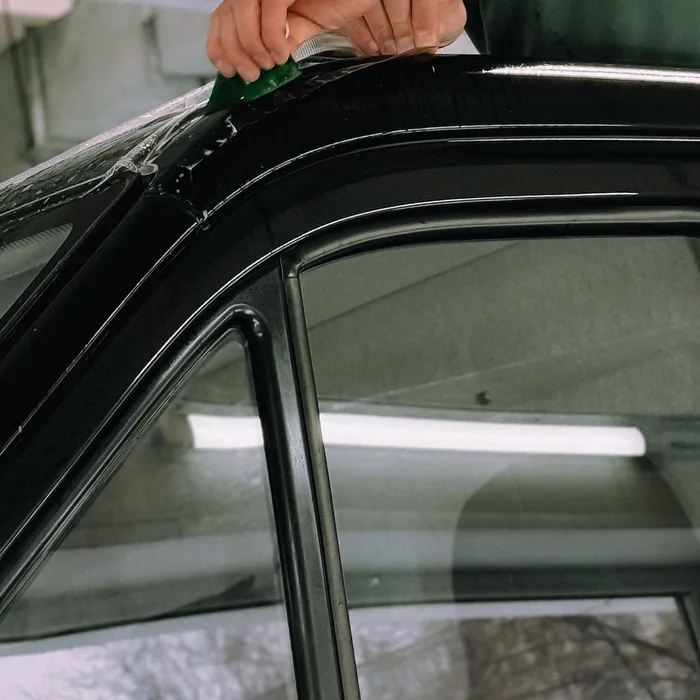 Installer applying ceramic window tint film to a vehicle roofline