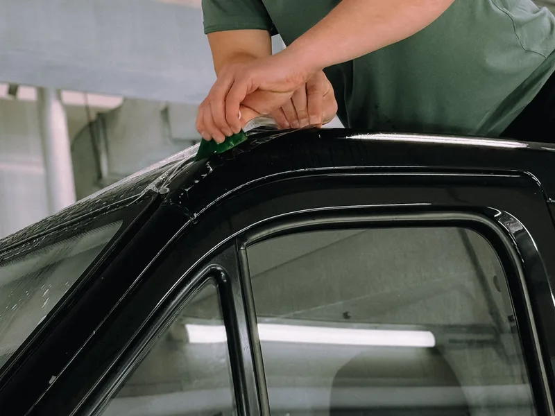 Installer applying ceramic window tint film to a vehicle